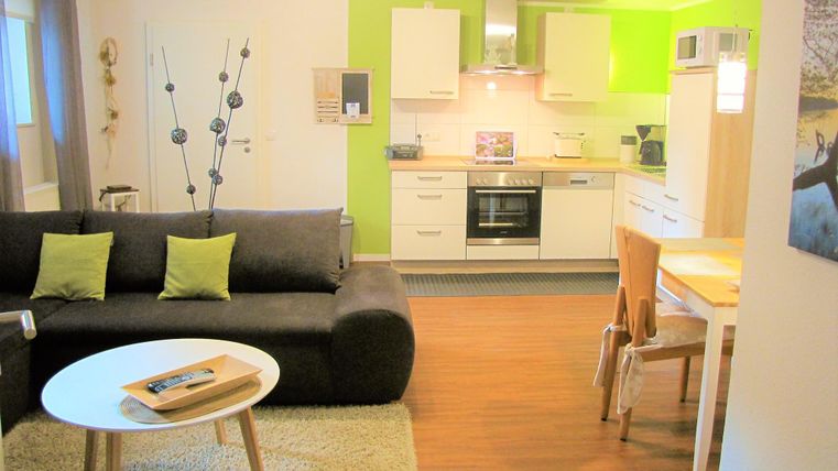 Eine moderne Wohnung mit einem gemütlichen Wohnzimmer und einer offenen Küche. Die Einrichtung ist hell und einladend, mit einem schlichten Tisch und Stühlen.