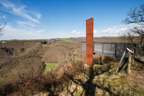Eine Aussichtsplattform mit einem modernen Steinsäulen-Monument. Im Hintergrund erstrecken sich sanfte Hügel unter einem klaren blauen Himmel.
