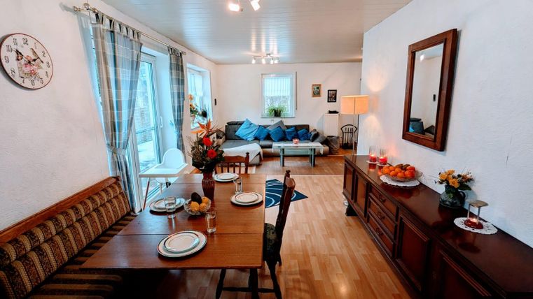 Ein gemütliches Wohnzimmer mit einem Essbereich und einem Sofa. Der Raum ist hell und einladend, mit Blumen und dekorativen Elementen.