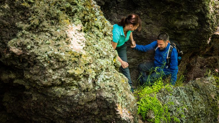 Ein Paar klettert über große Felsen in der Natur. Sie helfen sich gegenseitig beim Überwinden von Hindernissen.