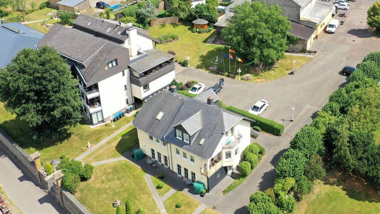 Ein Luftbild von Wohngebäuden in einer grünen Umgebung. Die Häuser sind von Bäumen und einem gepflegten Garten umgeben.