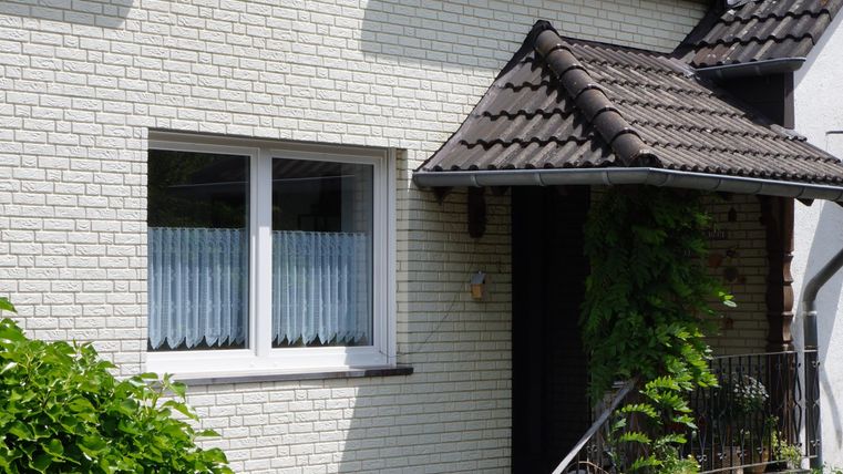 Ein gemütliches Einfamilienhaus mit einem gepflasterten Eingang. Der Garten ist schön angelegt und mit verschiedenen Pflanzen und Blumen dekoriert.