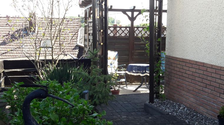 Ein gemütlicher Garten mit einem Tor und viel Grün. Im Hintergrund ist ein Tisch und Stühle zu sehen.