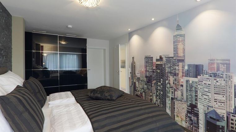 Ein modernes Schlafzimmer mit einem Bett in Schwarz und Weiß. Die Wand ist mit einem Stadtbild einer Skyline dekoriert.