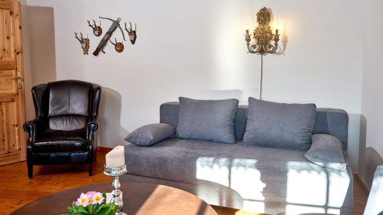 Ein modernes Wohnzimmer mit einem grauen Sofa und einem schwarzen Sessel. An der Wand hängen dekorative Elemente und es gibt einen Tisch mit einer Blumenvasen.