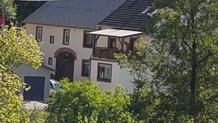 Ein charmantes Haus umgeben von Bäumen und Grün. Es hat einen Balkon und eine freundliche, einladende Atmosphäre.