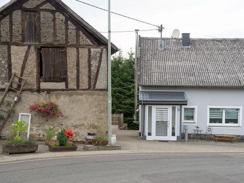 Ein traditionelles Fachwerkhaus und ein modernes Gebäude stehen an einer Straßenecke. Blühende Blumen zieren den Eingangsbereich.