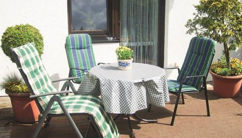 Een gezellige tuingelegenheid met een ronde tafel en vier stoelen. Op de tafel staat een bloempot en de omgeving is groen en uitnodigend.