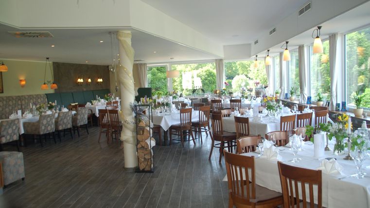 Ein elegantes Restaurant mit gedeckten Tischen und einem großen Fenster, das auf einen schönen Garten blickt. Die Einrichtung ist modern und einladend.