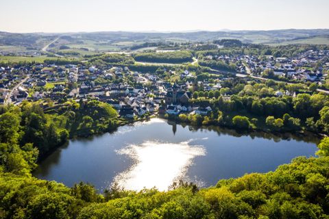 Eine malerische Landschaft mit einem ruhigen See und einer kleinen Stadt im Hintergrund. Üppige grüne Bäume umgeben das Wasser und bieten eine friedliche Atmosphäre.