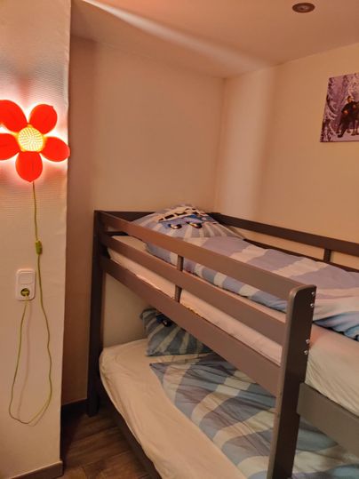 Ein gemütliches Zimmer mit einem Hochbett und einem bunten Blumenlicht. Die Bettwäsche ist blau und weiß.