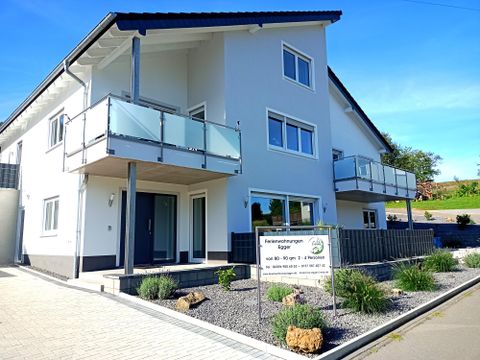 Ein modernes Wohngebäude mit zwei Etagen und Balkonen. Der Außenbereich ist gepflegt und mit Sträuchern sowie Steinen gestaltet.