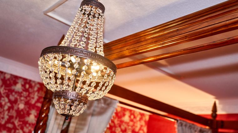 Ein eleganter Kronleuchter aus Kristall hängt von der Decke. Die Wände sind mit einem roten Blumenmuster dekoriert.