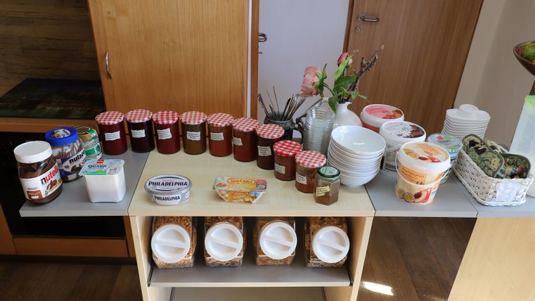 Ein Tisch mit verschiedenen Marmeladegläsern, Nutella und Schalen. Im Hintergrund stehen Blumen und andere Essensbehälter.