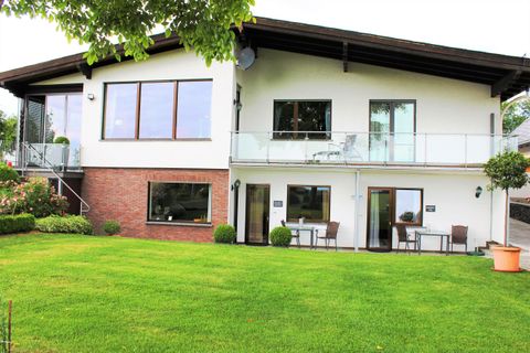 Ein modernes Haus mit einer großen Rasenfläche und einer Terrasse. Der Garten ist gepflegt und bietet eine einladende Atmosphäre.