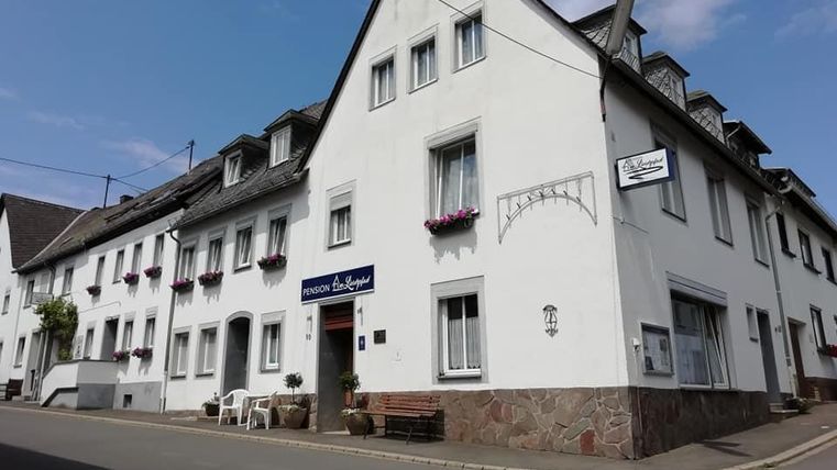 A white building with several windows and flower boxes. In front of the house, there are chairs and a table on the street.