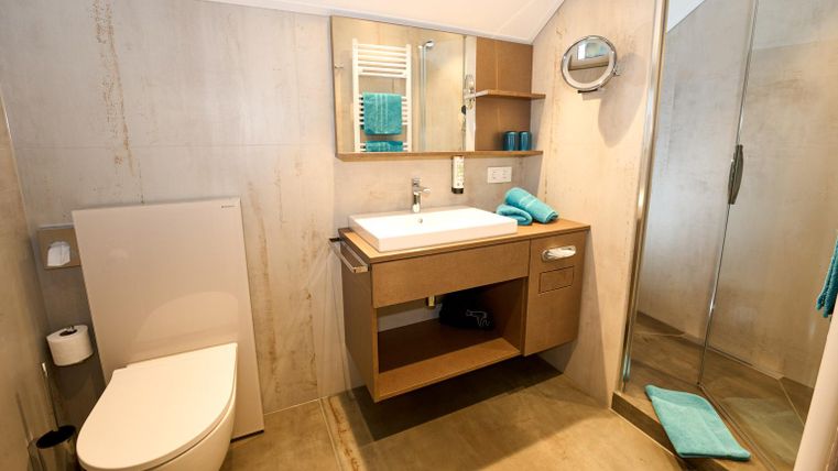 Ein modernes Badezimmer mit einer Dusche, einem Waschbecken und einem WC. Die Wände sind in neutralen Farben gehalten, und es sind einige Dekorationsgegenstände in Türkis vorhanden.