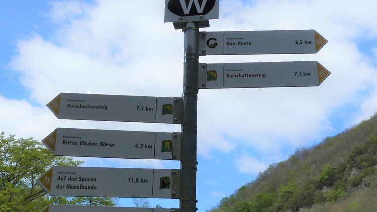 Ein Wegweiser mit mehreren Richtungsschildern. Die Schilder zeigen Entfernungen zu verschiedenen Zielen in der Umgebung an.