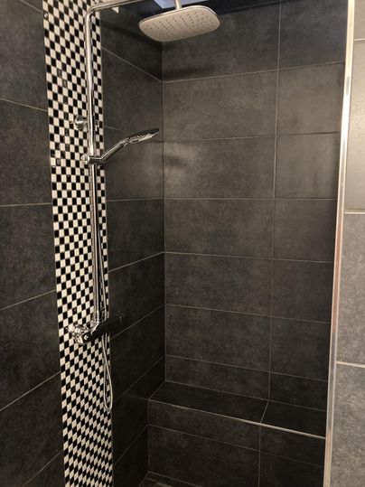 Eine moderne Dusche mit grauen Fliesen und einem schachbrettartigen Muster. Die Dusche ist mit einer Regendusche und einer handgeführten Duschbrause ausgestattet.