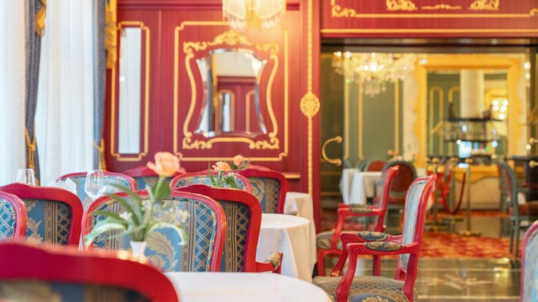Ein elegantes Restaurant mit roten Stühlen und dekorativen Wänden. Große Fenster sorgen für viel Licht und eine angenehme Atmosphäre.