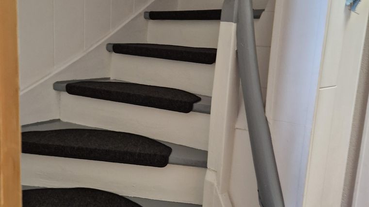Eine Treppe mit grauen Stufen und rutschfesten Trittflächen. Die Wände sind hell und der Handlauf ist elegant gestaltet.