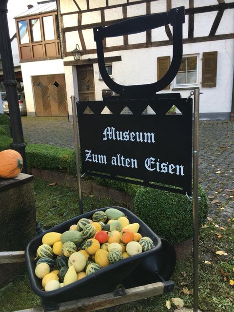 Ein Schild mit der Aufschrift "Museum Zum alten Eisen" steht vor einem historischen Gebäude. Im Vordergrund liegt eine Wanne mit bunten Kürbissen.