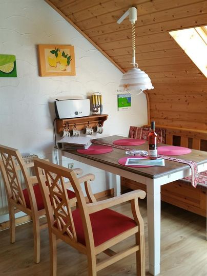 Ein gemütlicher Essbereich mit einem Holztisch und zwei Stühlen. Die Wände sind mit bunten Bildern geschmückt, und ein Fenster sorgt für viel Tageslicht.