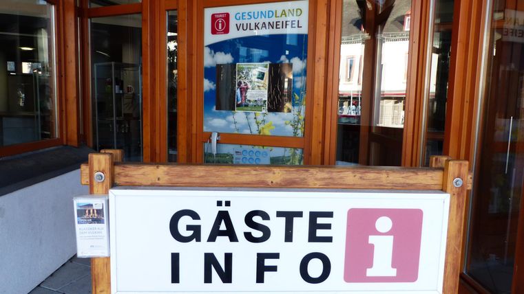 Ein Informationsschalter für Gäste mit dem Schild „GÄSTE INFO“. Im Hintergrund ist ein Plakat über die Region „Vulkanland“.