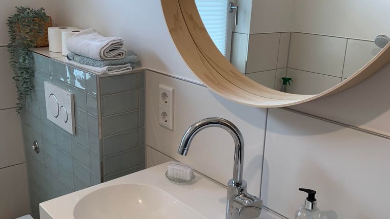 Ein modernes Badezimmer mit einem runden Spiegel und einem eleganten Waschbecken. Im Hintergrund sind Handtücher und eine kleine Pflanze zu sehen.