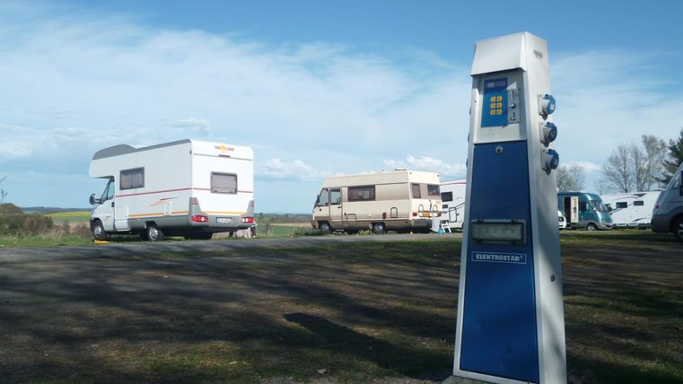 Eine Ladesäule für Elektrofahrzeuge steht auf einem Campingplatz. Im Hintergrund sind mehrere Wohnmobile zu sehen.
