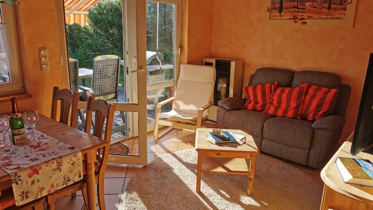 Ein gemütliches Wohnzimmer mit einem grauen Sofa und einem kleinen Tisch. Es gibt einen Esstisch aus Holz und viel Tageslicht, das durch die Fenster strömt.