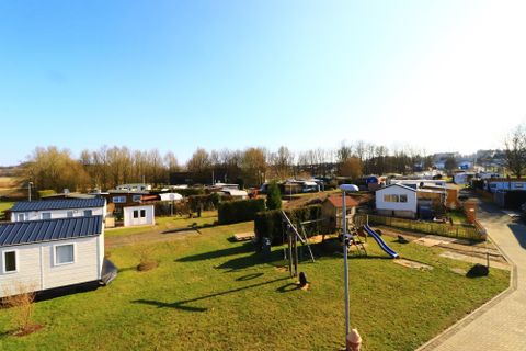 Eine idyllische Freizeitanlage mit mehreren Wohnmobilen und einem großen Grünbereich. Im Vordergrund gibt es Spielgeräte für Kinder und viel Sonnenlicht.