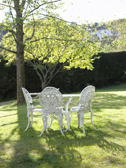 Ein hübscher Garten mit einem runden Tisch und vier weißen Stühlen. Bäume und grünes Gras schaffen eine einladende Atmosphäre.
