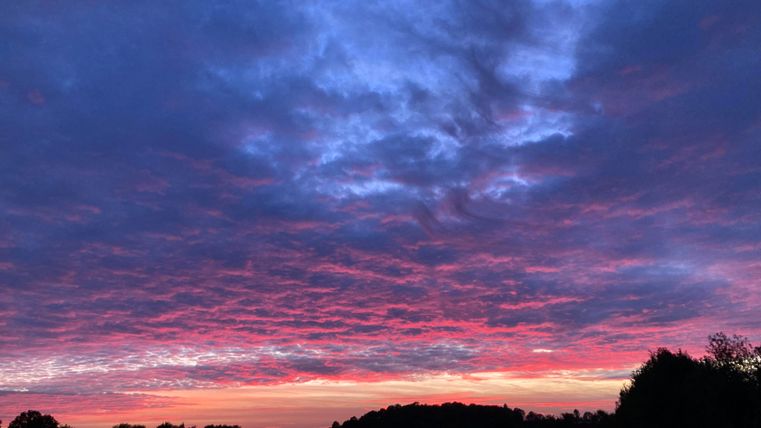Ein farbenfroher Sonnenuntergang mit violetten und rosa Wolken. Der Himmel strahlt in sanften Tönen über der Landschaft.