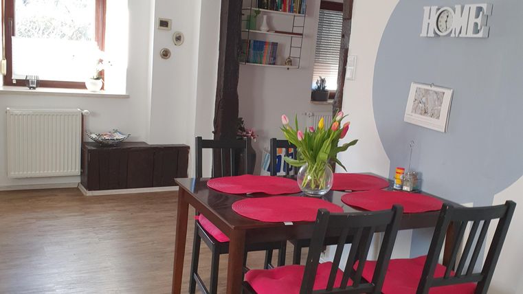 Ein gemütlicher Essbereich mit einem Tisch und Stühlen in Schwarz und Rot. An der Wand hängt das Wort "HOME" und es gibt eine helle Atmosphäre durch das Fenster.