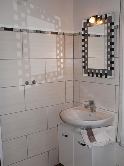 Ein modernes Badezimmer mit einer hellen Wandverkleidung und einem Waschbecken. Der Spiegel hat ein grafisches Design und es gibt eine Deckenleuchte.