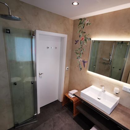 Ein modernes Badezimmer mit einer Glasdusche und einem eleganten Waschbecken. An der Wand sind dekorative Pflanzenmotive zu sehen.