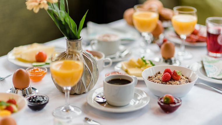 Ein üppiges Frühstückstisch mit verschiedenen Speisen. Es gibt Eier, Müsli, frisches Obst und Getränke.