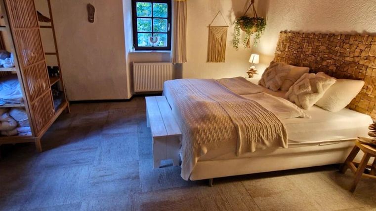 Ein gemütliches Schlafzimmer mit einem großen Bett, umgeben von warmem Licht. Der Raum hat eine natürliche Atmosphäre mit Holzdetails und Pflanzen.
