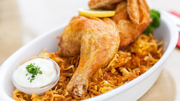 Ein köstliches Gericht mit knusprigem Hähnchen, serviert auf einem Bett aus Bratkartoffeln. Dazu gibt es eine Portion Sauce und frische Zitrone.