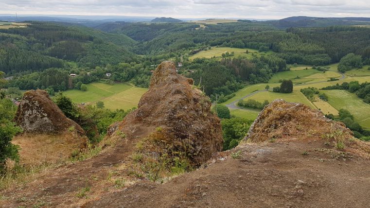 Eine Aussicht auf grüne Hügel und Täler unter einem bewölkten Himmel. Felsen erheben sich im Vordergrund und bieten einen Blick auf die Naturlandschaft.