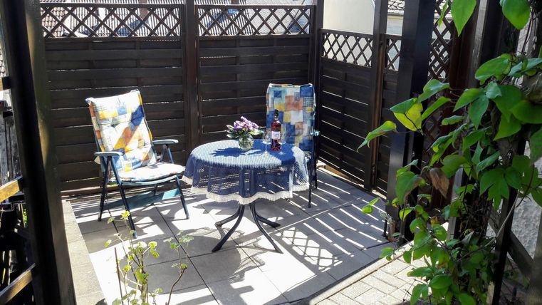 Eine gemütliche Terrasse mit zwei Stühlen und einem kleinen Tisch. Umgeben von grünen Pflanzen und einem Sichtschutz aus Holz.