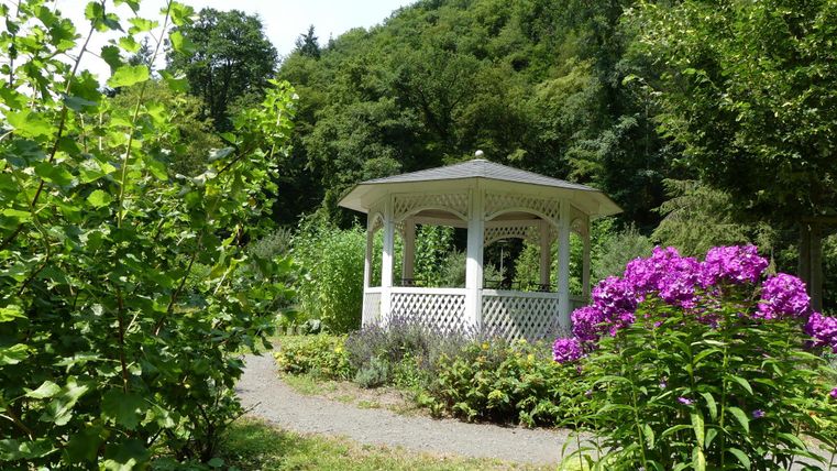 Ein hübsches Gartenpavillon umgeben von üppigem Grün und bunten Blumen. Der sonnige Ort lädt zum Entspannen ein.