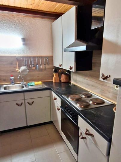 Eine moderne Küche mit hellen Schränken und einem dunklen Arbeitsbereich. Der Raum hat eine rustikale Holzdecke und ist gut beleuchtet.