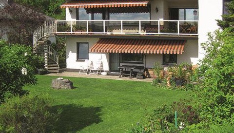 A well-maintained house with a green garden and a terrace. In the garden, there are chairs and a table, surrounded by plants.