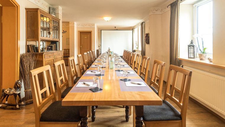 Ein großer Tagungsraum mit einem langen Holztisch und vielen Stühlen. Auf dem Tisch befinden sich Dekorationen und Notizblätter für die Teilnehmer.