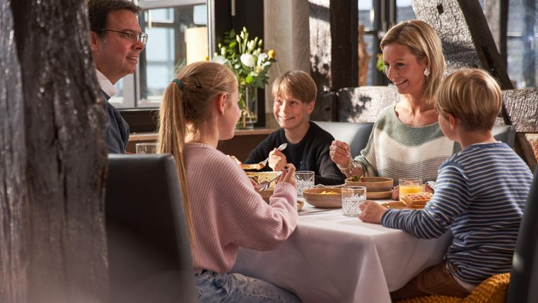Eine Familie sitzt gemeinsam am Tisch und genießt ein Essen. Sie lachen und haben eine angenehme Zeit miteinander.