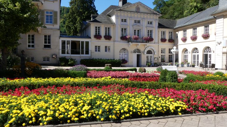 Ein schöner Garten mit bunten Blumenbeeten und einem eleganten Gebäude im Hintergrund. Die Atmosphäre ist einladend und freundlich.