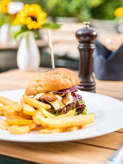 Ein saftiger Burger mit Salat, Käse und einer Scheibe Bacon. Dazu gibt es knusprige Pommes frites auf einem weißen Teller.