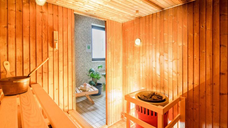 Eine gemütliche Sauna mit Holzpaneelen und warmem Licht. Im Hintergrund sieht man Grünpflanzen und einen offenen Zugang.